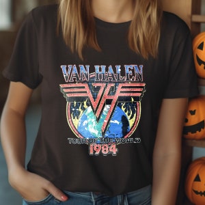 May include: A black t-shirt with a vintage-style graphic of Van Halen's "Tour of the World 1984" logo. The logo features a red, white, and blue "VH" symbol with flames and a globe.