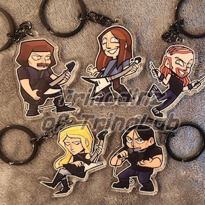 May include: Five acrylic keychains featuring cartoon-style illustrations of band members. Each keychain depicts a character with distinct hair and clothing, including guitarists and a vocalist, attached to a black metal split ring for keys.