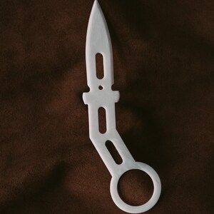 Könnte beinhalten: Weißes Plastikmesser mit einem Ringgriff. Das Messer ist wie ein Dolch geformt mit einer spitzen Spitze und einem abgerundeten Griff.