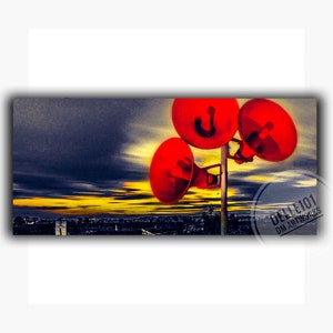 Op de afbeelding: Een artistieke afbeelding met drie rode megafoons op een paal tegen een dramatische lucht. De achtergrond toont een stadsgezicht met een levendige gele en oranje zonsondergang. Het kunstwerk is gesigneerd "DELLE101 DM ARTWORKS".
