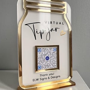 May include: A white acrylic sign shaped like a mason jar with a gold border. The sign says "Virtual Tip Jar" with a heart symbol. A QR code is in the centre of the sign. The sign also says "Thank you! ELW Signs & Designs".