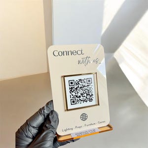 May include: A rectangular cream-coloured acrylic sign featuring the text Connect with us, a central square QR code framed in gold, a globe icon, and the text Lighting - Props - Furniture - Games. A small label at the base reads REMOVE FILM BEFORE USE.