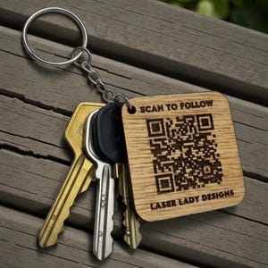 May include: A wooden keychain with a QR code and the text "SCAN TO FOLLOW" and "LASER LADY DESIGNS". The keychain is attached to a silver keyring with several keys.