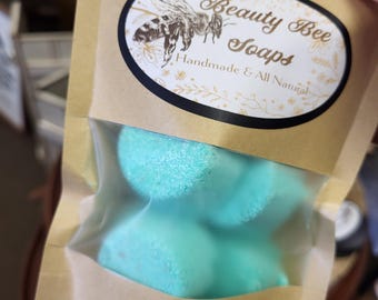 May include: A package of Beauty Bee Soaps, containing several light blue shower steamers. The package is made of brown paper with a clear window. The label features a bee illustration and the text "Handmade & All Natural". The bottom label reads "All Natural Shower Steamers: Lavender Eucalyptus".