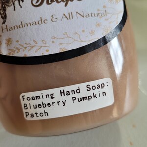 May include: A bottle of foaming hand soap with a light brown hue. The label reads "Beauty Soaps, Handmade & All Natural." The product is scented with Blueberry Pumpkin Patch.