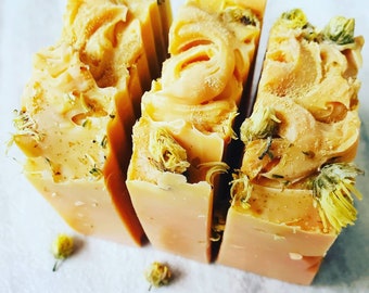 May include: Four bars of handmade soap with a light yellow color and a swirl design. The soap is decorated with dried flowers.