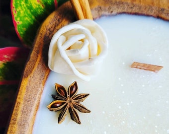 May include: A white candle in a wooden bowl with a white rose, star anise, and cinnamon sticks on top.