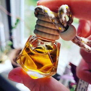 May include: A small, clear glass bottle with a gold and brown wooden stopper. The bottle is filled with a golden liquid and has a string attached to the stopper.