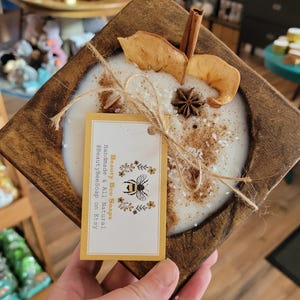 May include: A wooden tray with a white candle, cinnamon stick, dried apple slices, and star anise. The candle is topped with a sprinkle of salt. A yellow tag with the text "Beauty Bee Soaps Handmade & All Natural BeautyBeeSoap on Etsy" is attached to the tray.