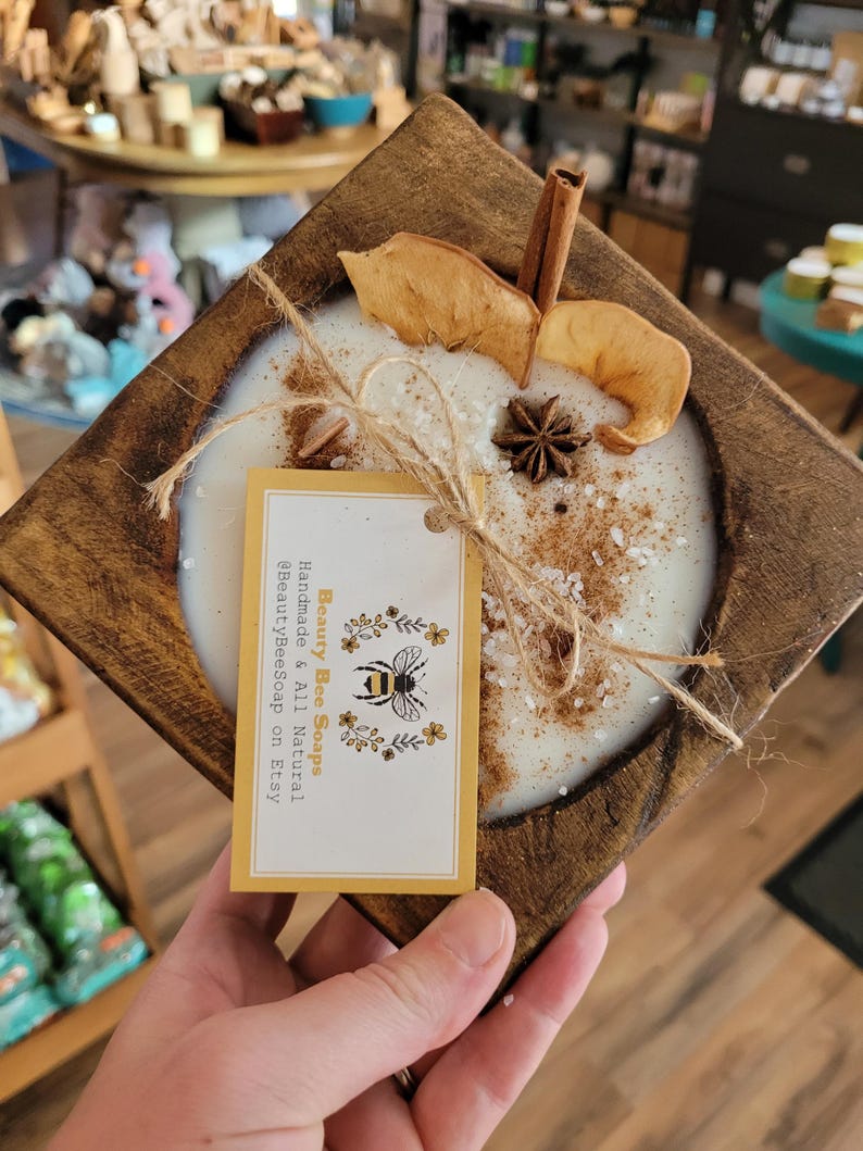 May include: A wooden tray with a white candle, cinnamon stick, dried apple slices, and star anise. The candle is topped with a sprinkle of salt. A yellow tag with the text "Beauty Bee Soaps Handmade & All Natural BeautyBeeSoap on Etsy" is attached to the tray.