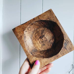 May include: A square wooden bowl with a deep, rounded interior. The bowl is made of dark brown wood with a natural wood grain pattern.