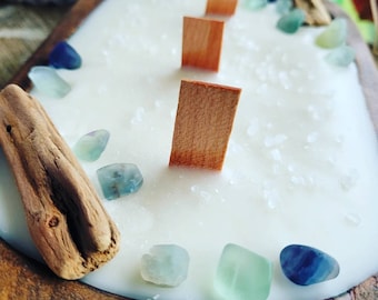 May include: A white candle in a wooden bowl with wooden wicks and blue and green crystals. The candle is surrounded by sea salt.