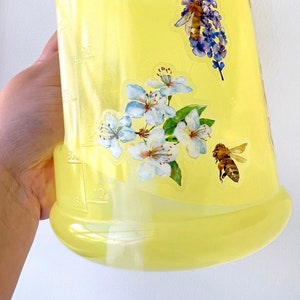 以下が含まれることがあります： 透明な液体が入った黄色のプラスチックボトル。ボトルには、蜂と花が描かれたステッカーが貼られており、ステッカーには「things you wish to see」という文字が書かれています。