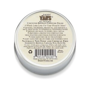 May include: A round, silver-colored tin of Daddy Van's Unscented Beeswax Furniture Polish. The label features text describing the product's benefits, including renewing and protecting wood surfaces. The product is made in Fairview, NC, USA.