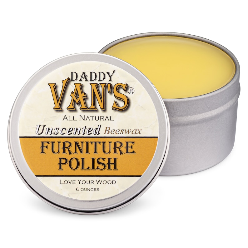 May include: An open, round, silver tin of Daddy Van's All Natural Unscented Beeswax Furniture Polish. The tin's lid is next to the open tin, revealing the yellow polish. The label reads "Love Your Wood" and contains 6 ounces of product.