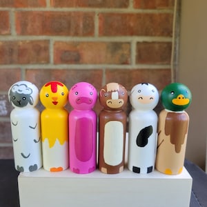 May include: Six hand-painted wooden peg dolls in the shape of farm animals. The set includes a sheep, chicken, pig, monkey, cow, and duck. Each doll is painted with bright colors and detailed features, standing on a white wooden base.