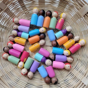 May include: A basket filled with colourful wooden peg dolls. The dolls are painted in various shades of pink, blue, green, orange, yellow, and brown. The dolls are arranged in a circular pattern.