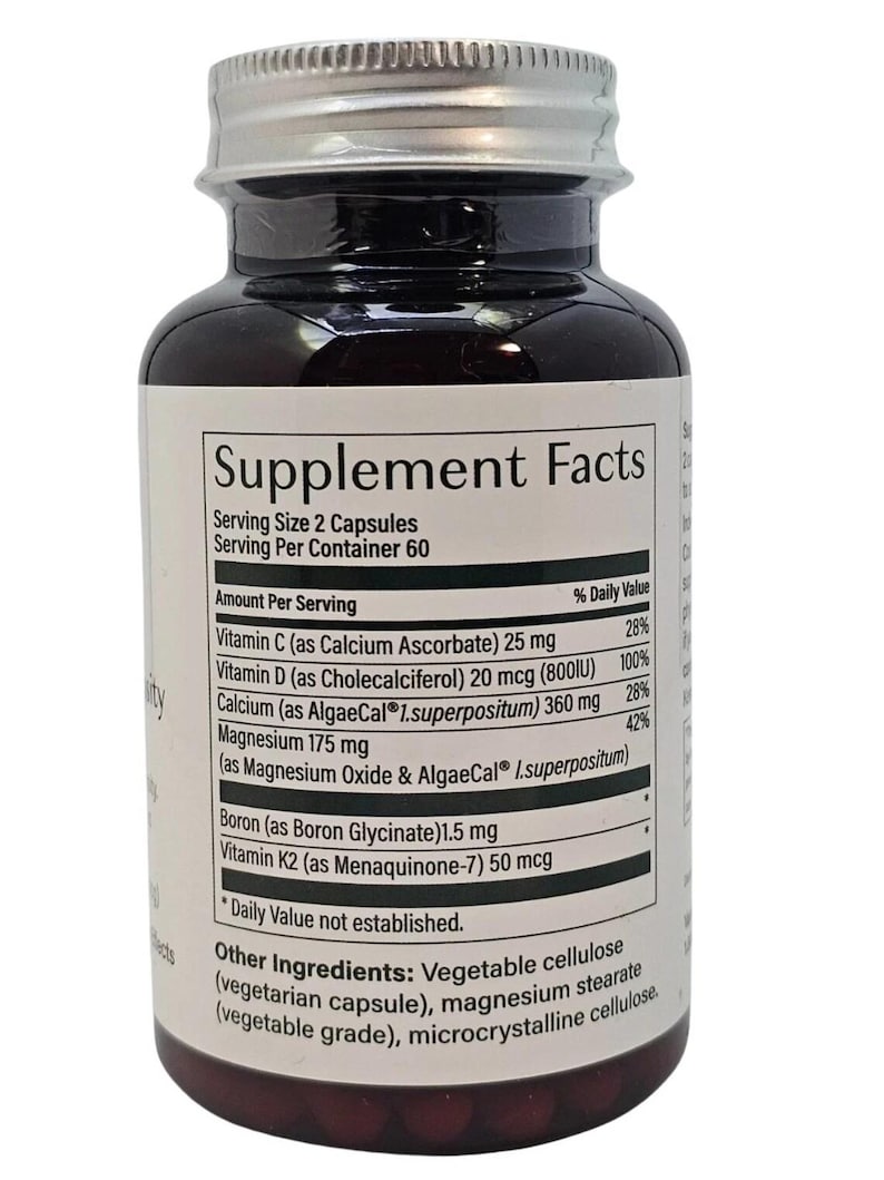 Puede incluir: Una botella de suplemento marr&oacute;n oscuro con tapa plateada. La etiqueta muestra "Supplement Facts" y enumera vitaminas y minerales, incluyendo vitamina C, D, calcio y magnesio. La botella contiene 60 porciones, con una porci&oacute;n de 2 c&aacute;psulas.