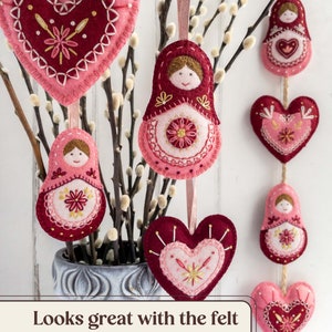 In the foreground, two wool felt heart ornaments are hanging from pussy willow branches with two felt Matryoshka doll ornaments. More felt hearts and dolls are strung on a garland in the background. Overlaid text reads "Looks great with the felt Matryoshka dolls!".