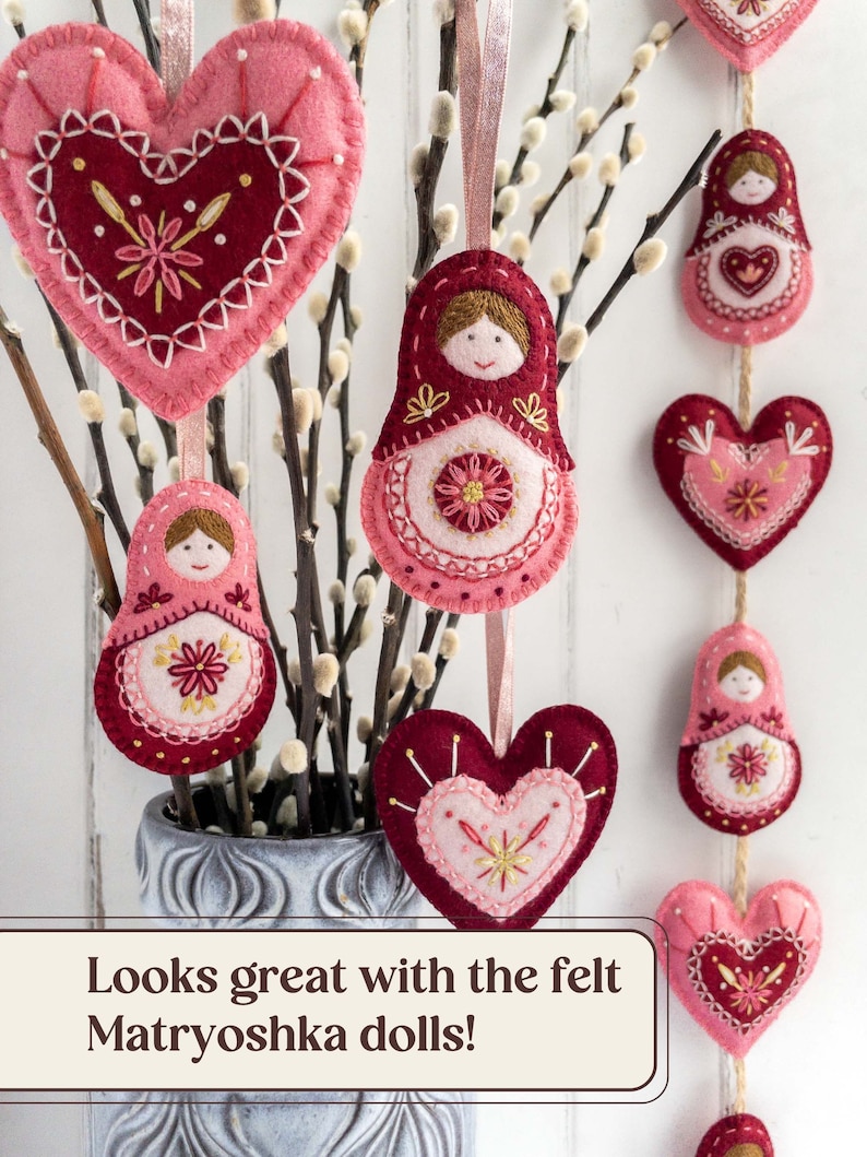 In the foreground, two wool felt heart ornaments are hanging from pussy willow branches with two felt Matryoshka doll ornaments. More felt hearts and dolls are strung on a garland in the background. Overlaid text reads "Looks great with the felt Matryoshka dolls!".
