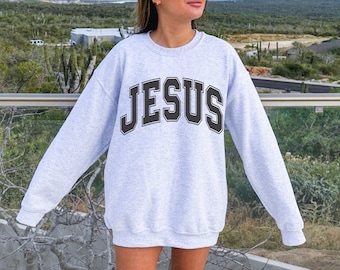 May include: A gray sweatshirt with the word "JESUS" printed in black block letters on the front.