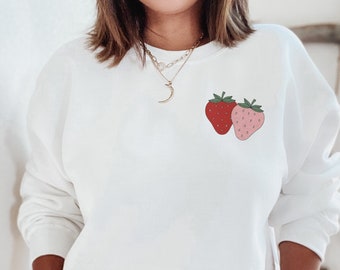 Peut inclure: Sweat-shirt blanc avec un motif de fraises rouge et rose sur le devant.