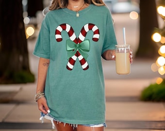 May include: A teal blue t-shirt with a graphic of two red and white candy canes tied together with a green bow.