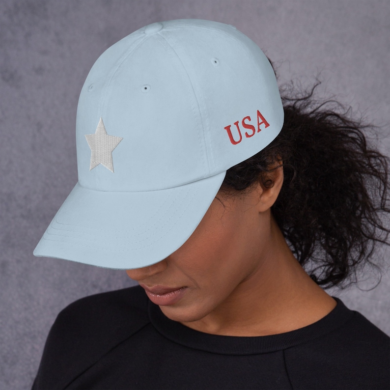 Pode incluir: Um bon&eacute; de beisebol azul claro com uma estrela branca e a palavra "USA" bordada em vermelho na frente.