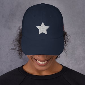 Pode incluir: Um bon&eacute; de beisebol azul marinho com uma estrela branca bordada na frente. O bon&eacute; tem uma aba curva e uma correia ajust&aacute;vel.