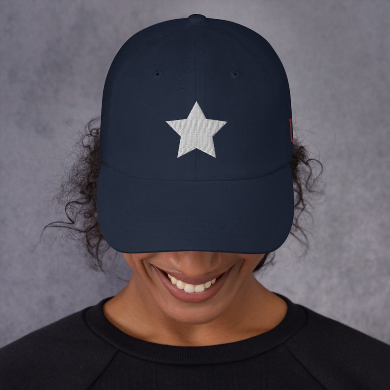Pode incluir: Um bon&eacute; de beisebol azul marinho com uma estrela branca bordada na frente. O bon&eacute; tem uma aba curva e uma correia ajust&aacute;vel.