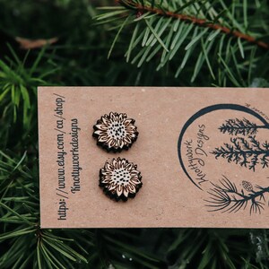 May include: A pair of wooden sunflower earrings on a brown card with the text "Knottywork Designs" and a website address. The earrings are made of wood and have a natural finish.
