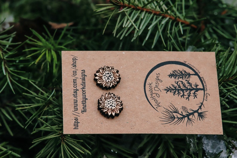 May include: A pair of wooden sunflower earrings on a brown card with the text "Knottywork Designs" and a website address. The earrings are made of wood and have a natural finish.