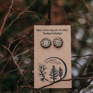 May include: A pair of wooden sunflower earrings on a brown card with the text "https://www.etsy.com/ca/shop/Knottyworkdesigns" and "Knottywork Designs".