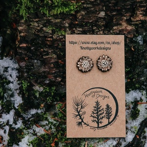 May include: A pair of wooden earrings with a sunflower design. The earrings are on a brown card with the text "Knottywork Designs" and a website address.