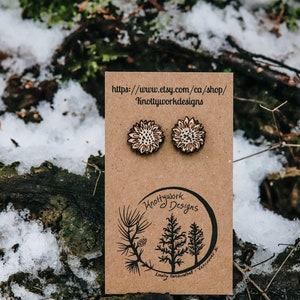 May include: A pair of wooden sunflower earrings on a brown card with the text "Knottywork Designs" and a website address. The earrings are locally handcrafted in Vancouver, BC.