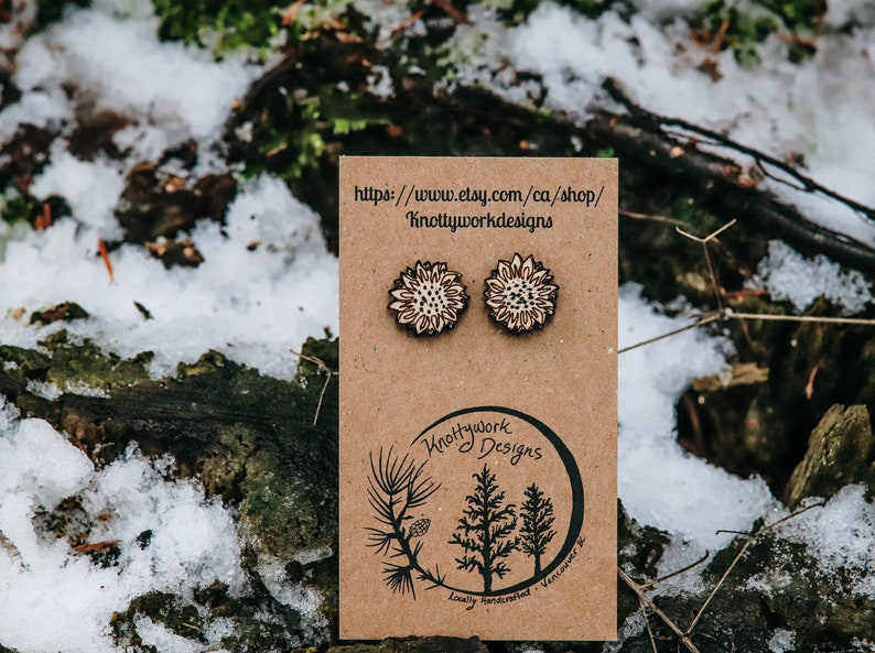 May include: A pair of wooden sunflower earrings on a brown card with the text "Knottywork Designs" and a website address. The earrings are locally handcrafted in Vancouver, BC.
