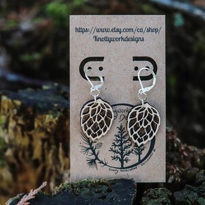 May include: A pair of wooden earrings shaped like a hop cone, with silver hooks. The earrings are displayed on a brown card with the text "https://www.etsy.com/ca/shop/Knottyworkdesigns" and "Lovely handcrafted - Vancouver, BC".