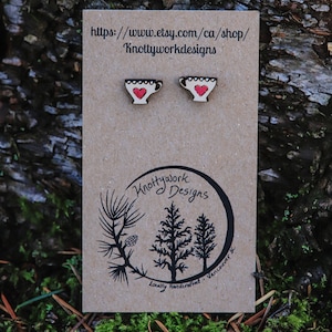 Op de afbeelding: Een paar houten oorbellen in de vorm van theekopjes met rode harten. De oorbellen worden getoond op een bruine kaart met de tekst "Knottywork Designs" en "Lokaal handgemaakt - Vancouver BC".