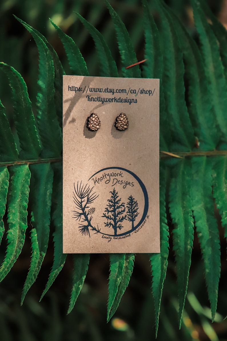 K&ouml;nnte beinhalten: Ein Paar Holz-Kiefernzapfen-Ohrringe auf einer braunen Karte mit dem Text "Knottywork Designs" und der Website-Adresse "https://www.etsy.com/ca/shop/Knottyworkdesigns".