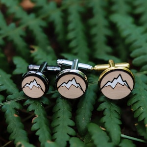 May include: Three pairs of cufflinks featuring a mountain design. The cufflinks are made of wood and metal. The metal is silver, gold, and black.