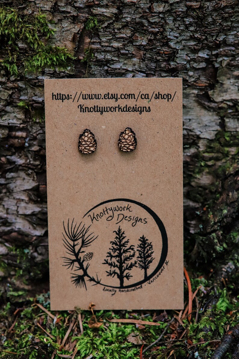 K&ouml;nnte beinhalten: Ein Paar Holz-Kiefernzapfen-Ohrringe auf einer braunen Karte mit dem Text "Knottywork Designs" und der Website-Adresse "https://www.etsy.com/ca/shop/Knottyworkdesigns".