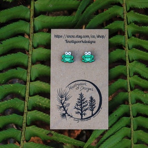 May include: A pair of green frog stud earrings on a brown card with the text "Knottywork Designs" and a website address.