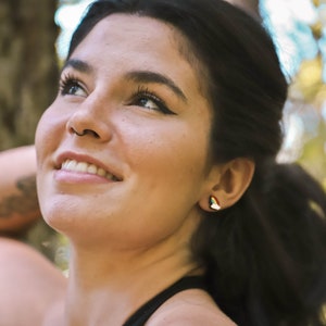 Pu&ograve; includere: Una donna con lunghi capelli scuri sorride e guarda il cielo. Indossa una canotta nera e ha un piccolo orecchino all'orecchio sinistro.