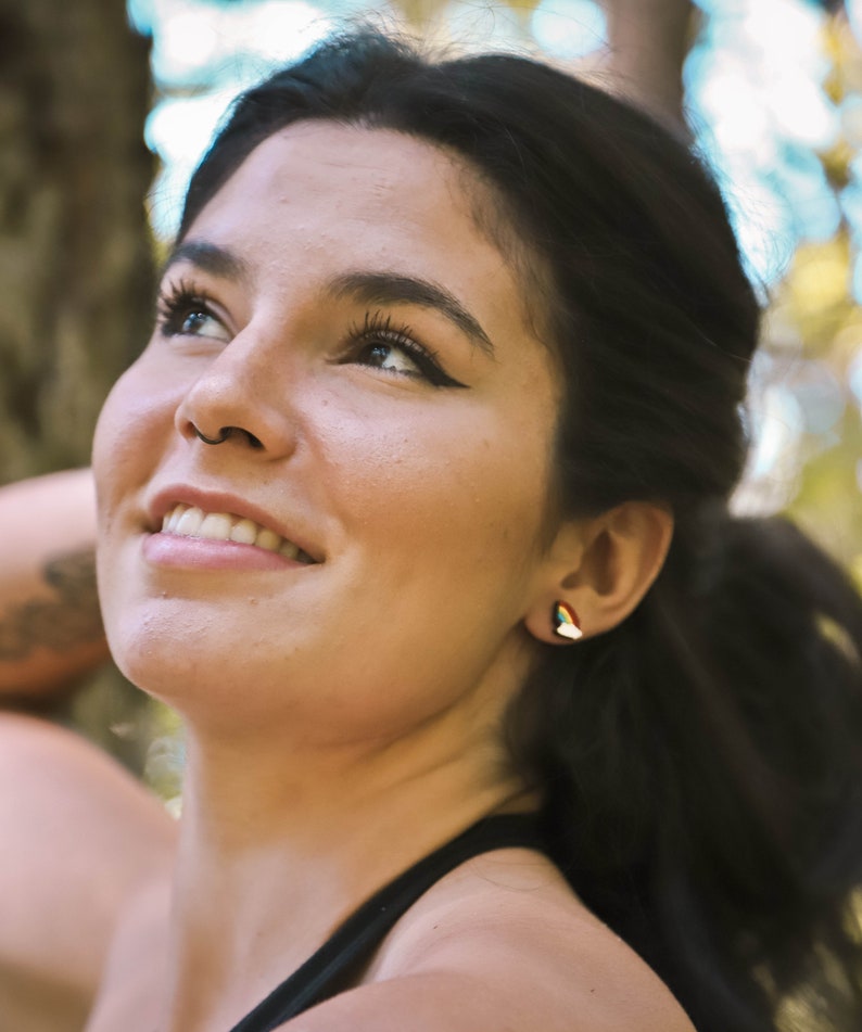 Pu&ograve; includere: Una donna con lunghi capelli scuri sorride e guarda il cielo. Indossa una canotta nera e ha un piccolo orecchino all'orecchio sinistro.