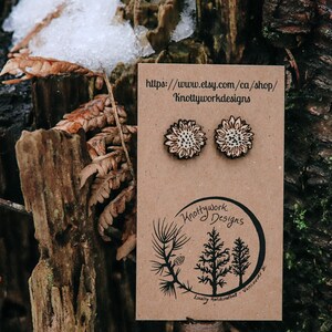May include: A pair of wooden sunflower earrings on a brown card with the text "Knottywork Designs" and a website address. The earrings are locally handcrafted in Vancouver.