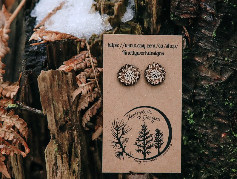 May include: A pair of wooden sunflower earrings on a brown card with the text "Knottywork Designs" and a website address. The earrings are locally handcrafted in Vancouver.