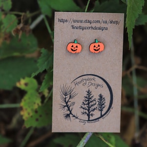 Può includere: Un paio di orecchini a forma di zucca in legno arancione e verde su una carta marrone con il testo "https://www.etsy.com/ca/shop/Knottyworkdesigns" e un logo con il testo "Knottywork Designs".