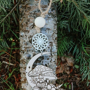 Peut inclure: Une décoration en bois représentant une lune croissante avec un champignon et des fleurs, un attrape-rêves et une perle en bois blanche. La décoration est suspendue à un morceau de ficelle.