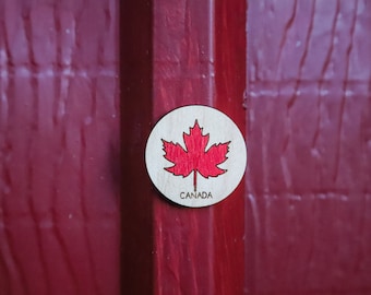 Op de afbeelding: Een rond houten bord met een rood esdoornblad en het woord "CANADA" eronder.