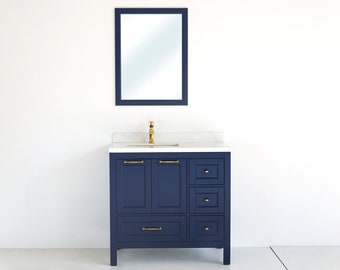 May include: A navy blue bathroom vanity with a white countertop and a gold faucet. The vanity has three drawers and two doors. A rectangular mirror with a gold frame is mounted above the vanity.